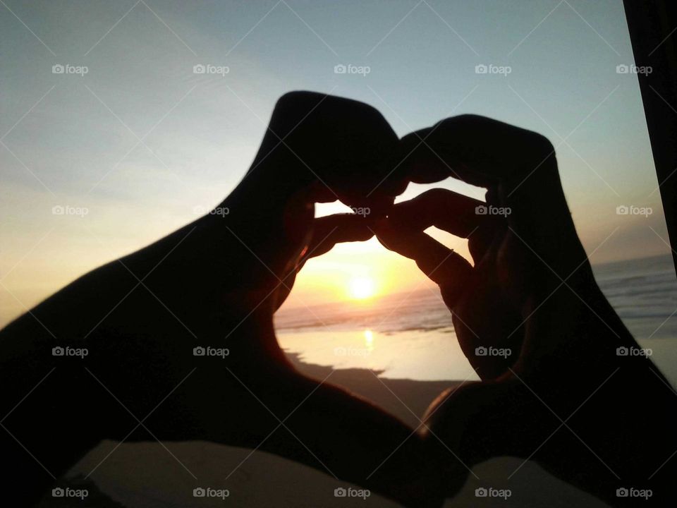 Beautiful sunset trough heart made of human hands.