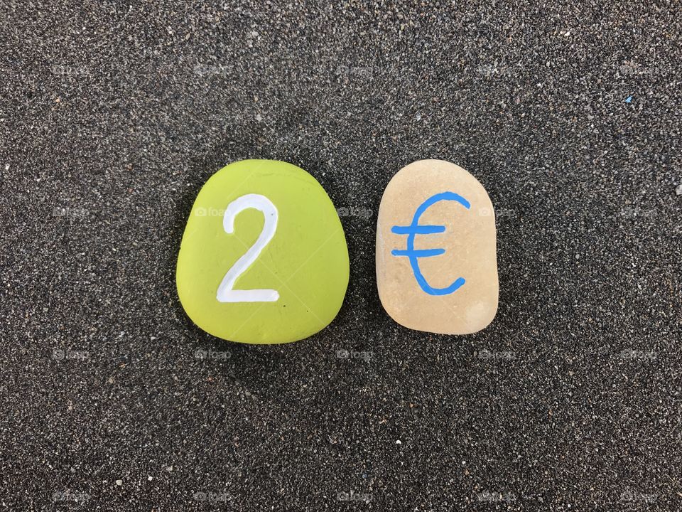 2 Euro with colored stones over black volcanic sand