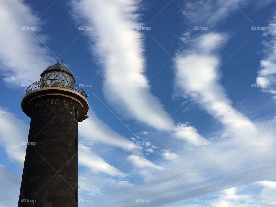 Top of light house in front of clouds with blue sky