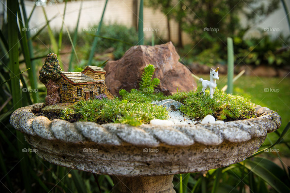 Small garden pot in backyard with miniature stone house and unicorn, grass and mini trees. Diy garden pot ideas for small places
