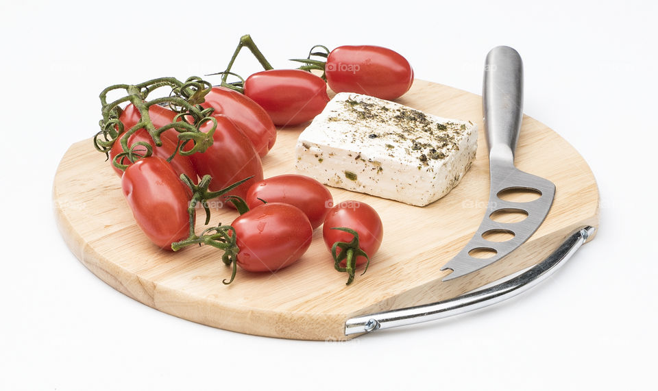 Savoury Roma tomatoes, feta  cheese and knife on a cutting board  isolated against a white bacground.