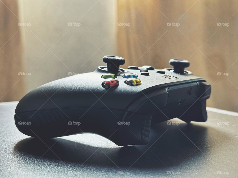 Black Xbox controller situated on a wood table while the light enters through the window.