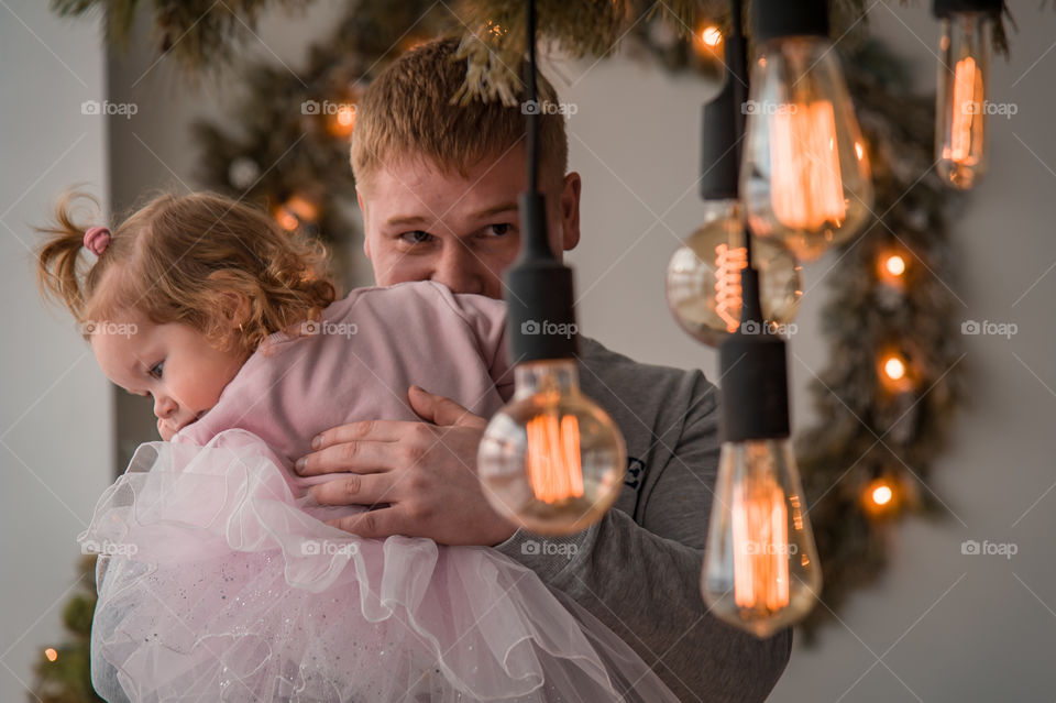 dad with a daughter in his arms on the background of Christmas decorative diode lamps