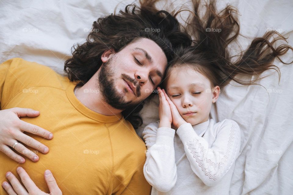 Young sleeping family with bearded father and daughter on bed in cozy home, view from top