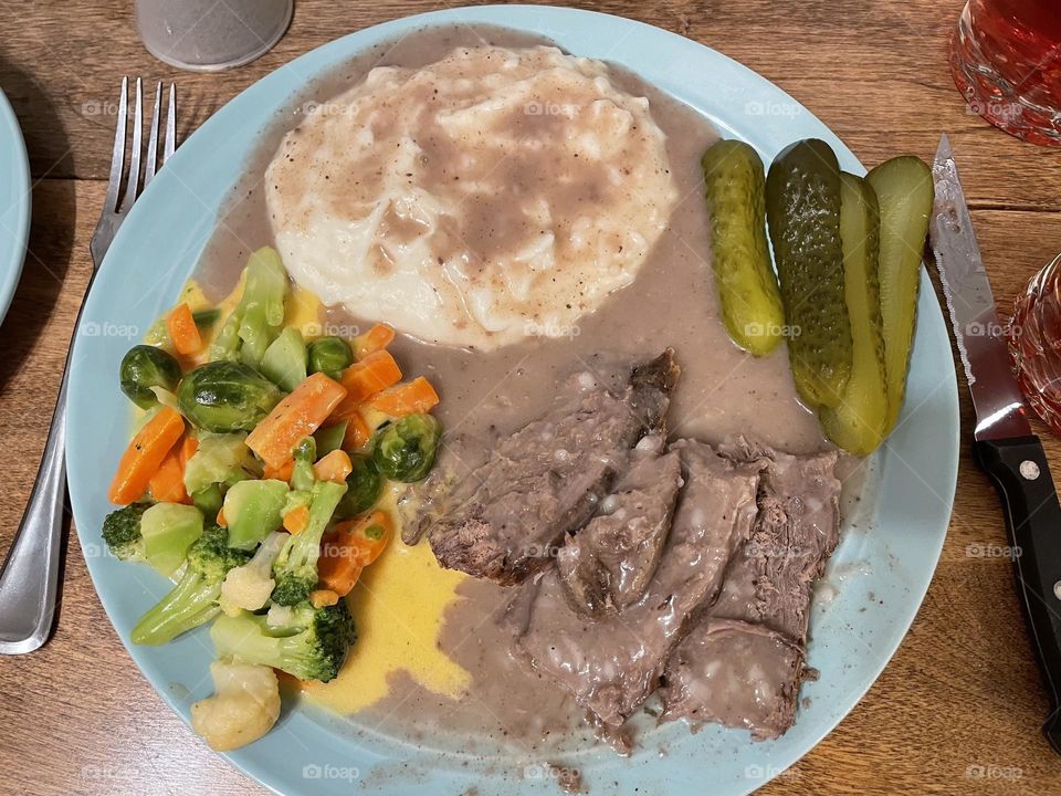 Delicious homemade supper, including slow cooked beef roast, mashed potatoes and gravy, steamed mixed veggies with cheese sauce and dill pickles on the side