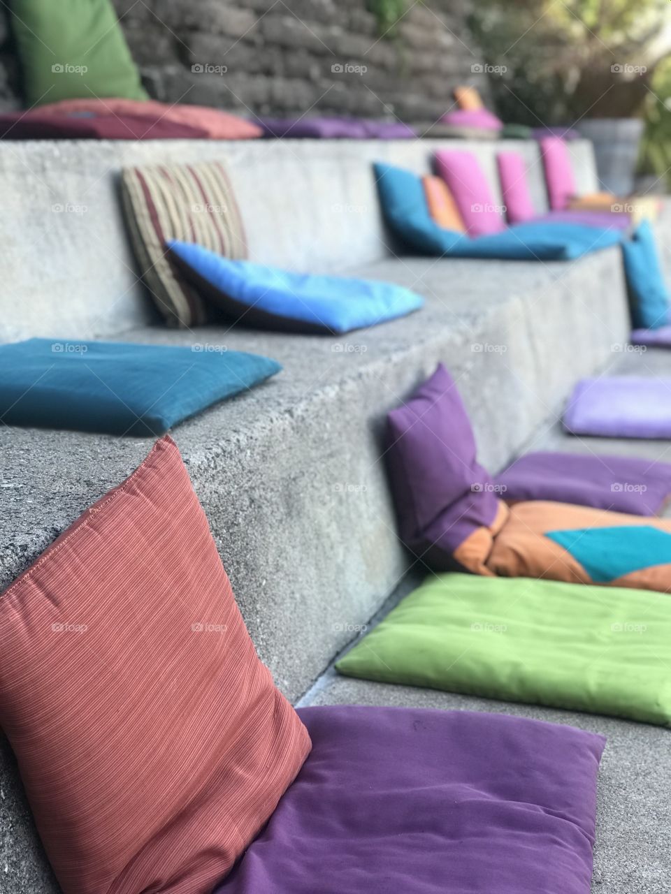 Colorful pillows and cushions thrown strategically against  large cement steps to creat a cozy seating area for guests at a restaurant. 