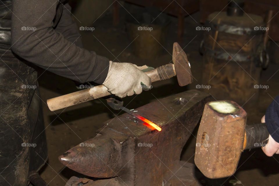 A blacksmith on an anvil makes metal products from red-hot material.  Blacksmith workshop