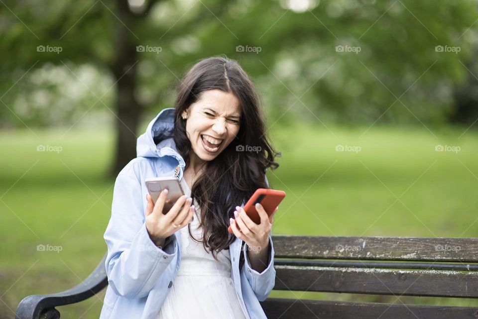 Emotional woman with two phones on a park bench