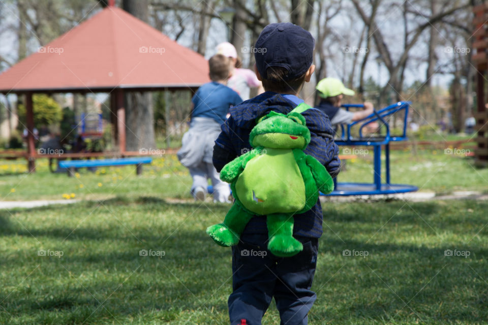 Small young boy in a park. with his frog bag on his back
