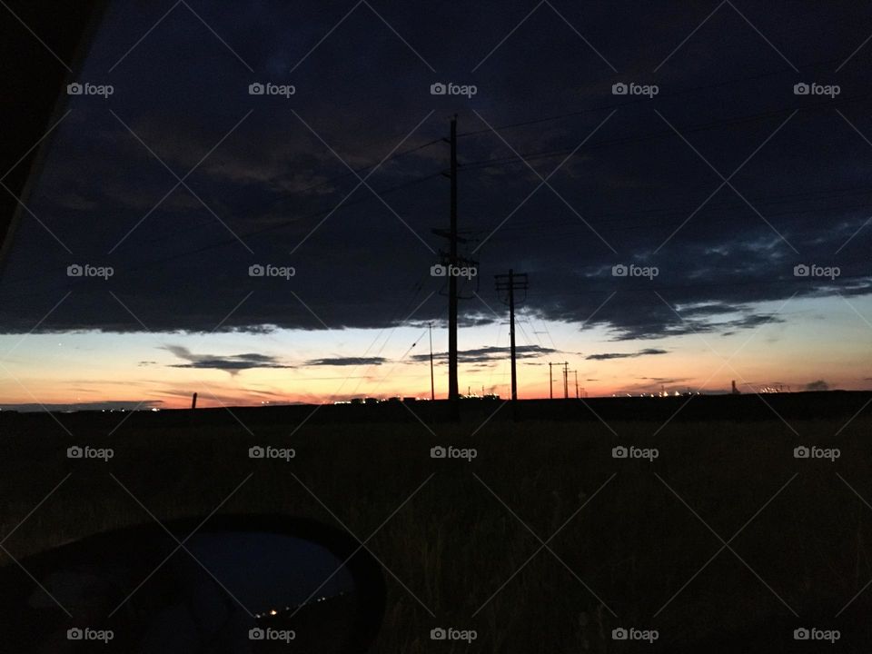 Dark black clouds, dark landscape as the sun just setting in the clear sky beyond
