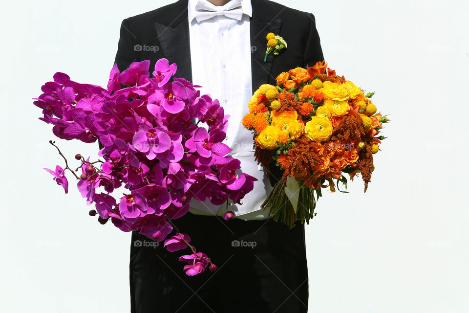 Groom with 2 flower bouquets . Groom in black tuxedo holds one bright colorful flower bouquet in each hand on his wedding day