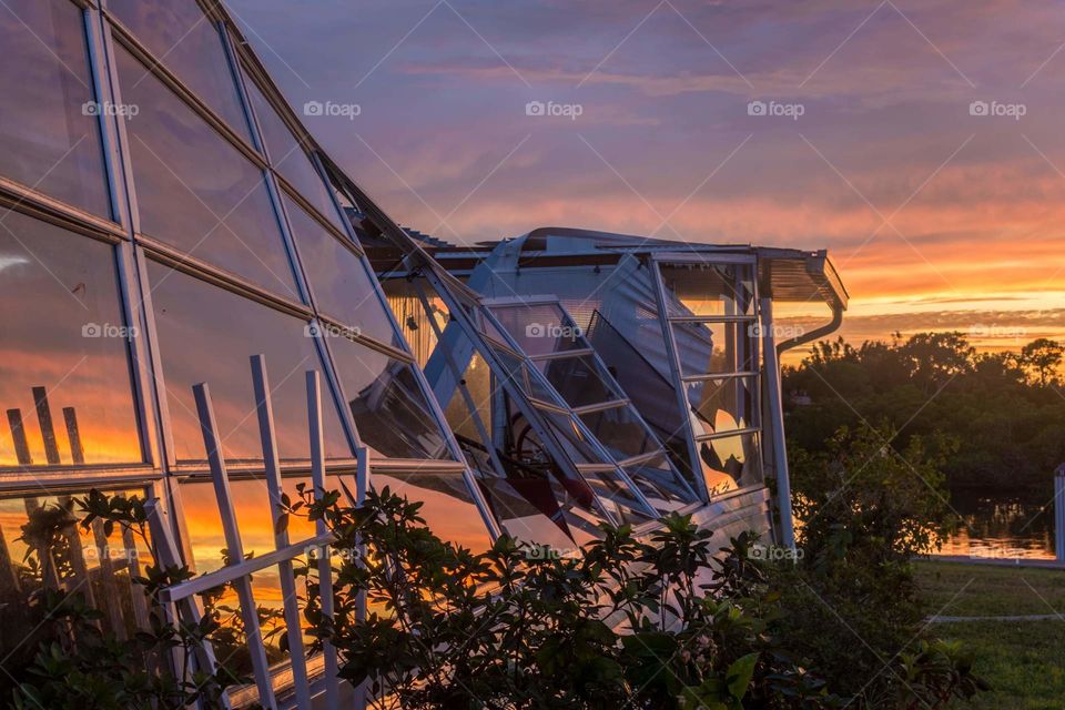 smashed windows from hurricane destruction reflecting the orange and purple colors of the sunset are sad but breathtakingly beautiful