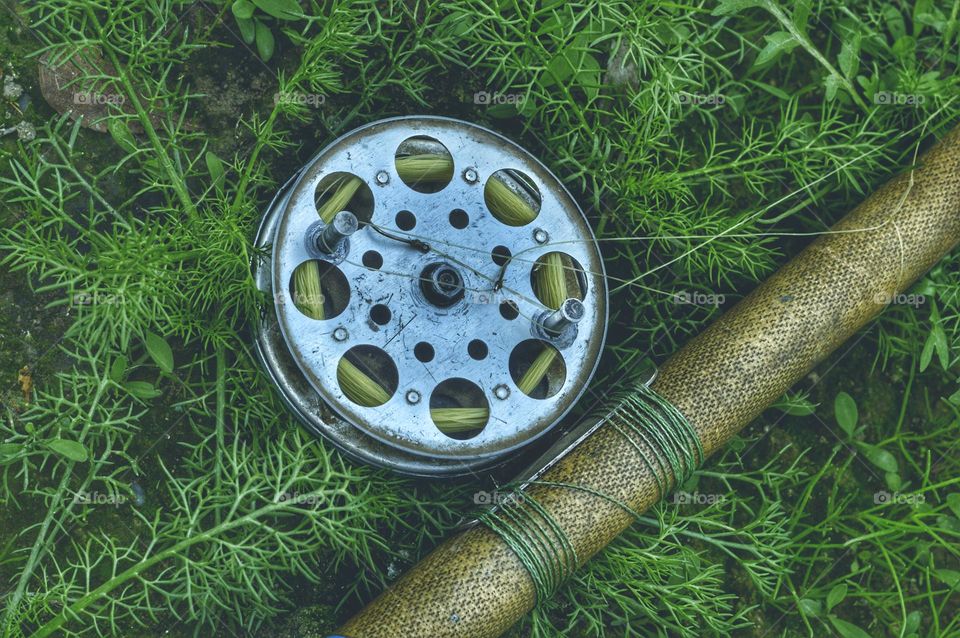an old vintage spinning rod with a reel lies on the grass. drum with circles and fishing line. the body of the fishing rod is fiberglass.