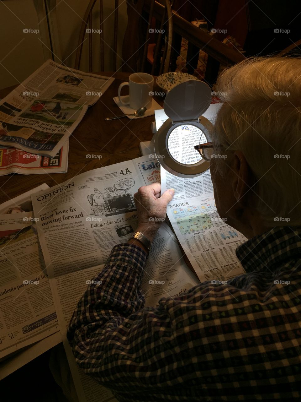 Elderly older senior citizen man reading newspaper with lighted magnifying glass