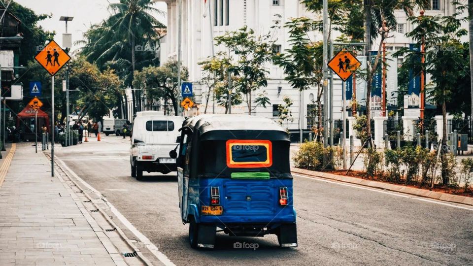 Portrait of a blue tuk-tuk stopping on a quiet city street. Around it there are pedestrian crossing signs and warnings of children playing