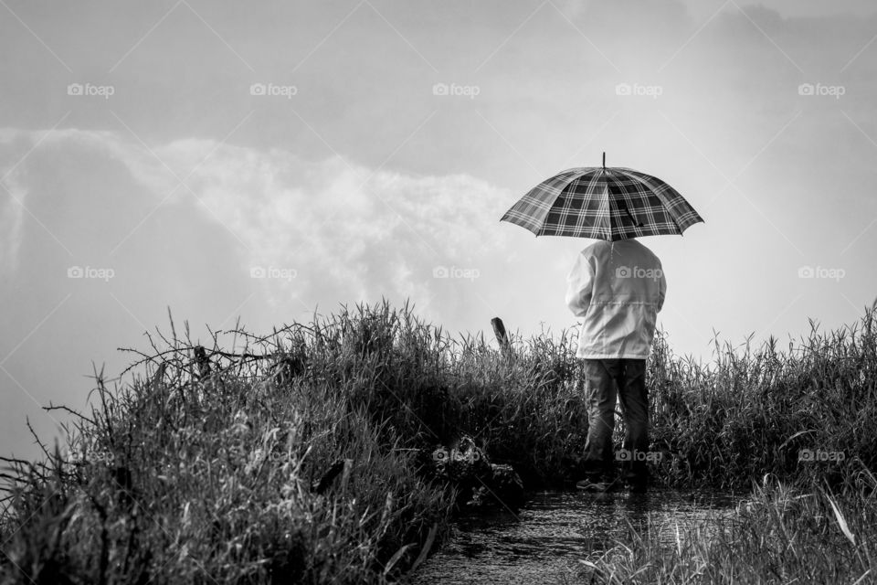 Moment of contemplation. Black and white image of man standing with umbrella while the waterfall mist rains down and the sound of the water drowns out all noise.