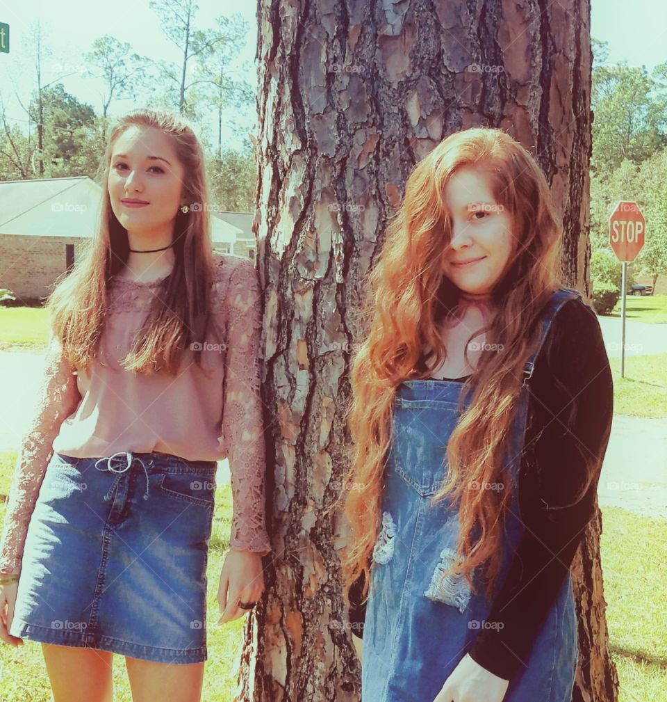 Two beautiful girls standing under a pine tree in the fall weather