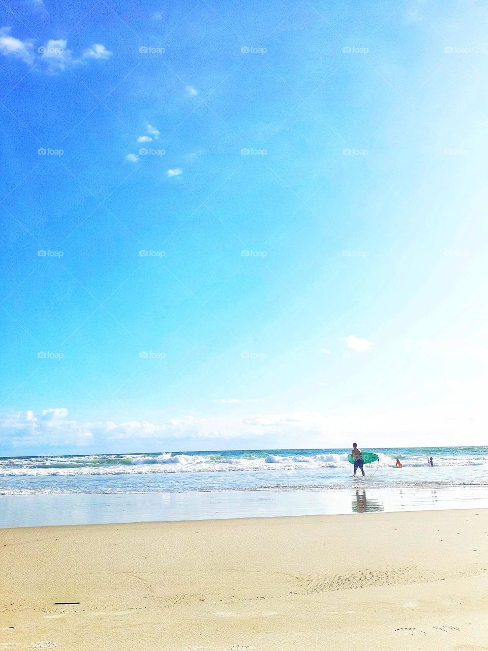 A surfer carries a surfboard into the ocean for a day of surfing at Ponce Inlet Beach.