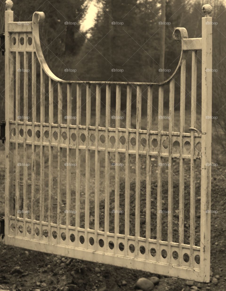 Sepia toned photo of old wrought iron fence that opens up to an open field. 