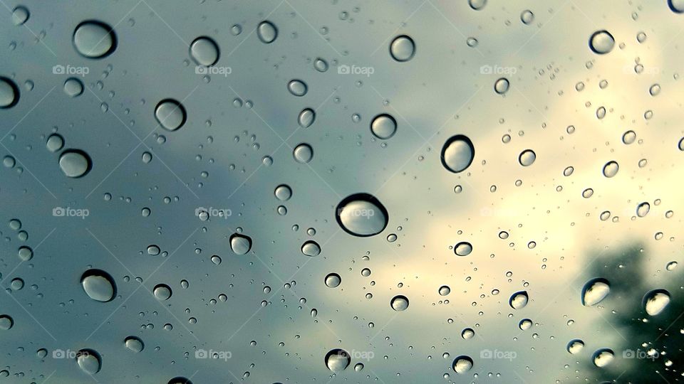 Raindrops on windshield of car after bad storm with sky in background.