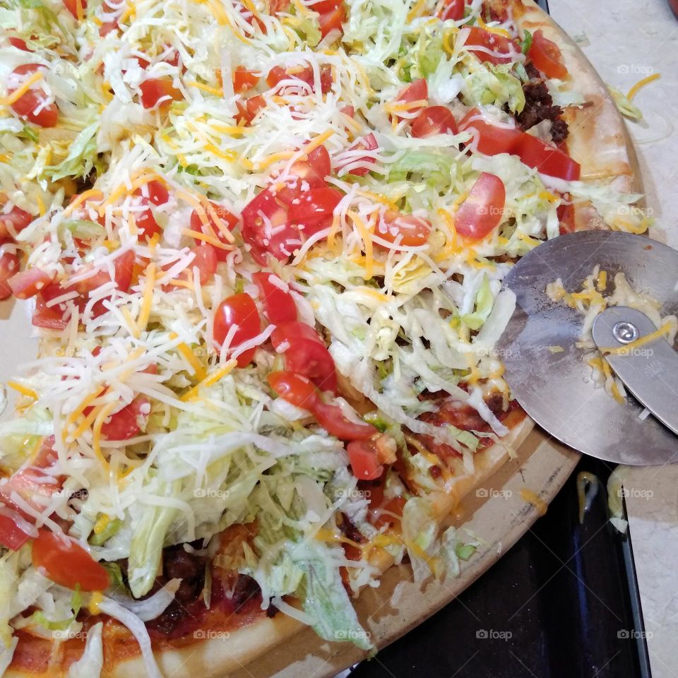 A taco pizza with tomatoes, lettuce, meat, cheese, and sauce on homemade crust that I had at a friend's birthday party.