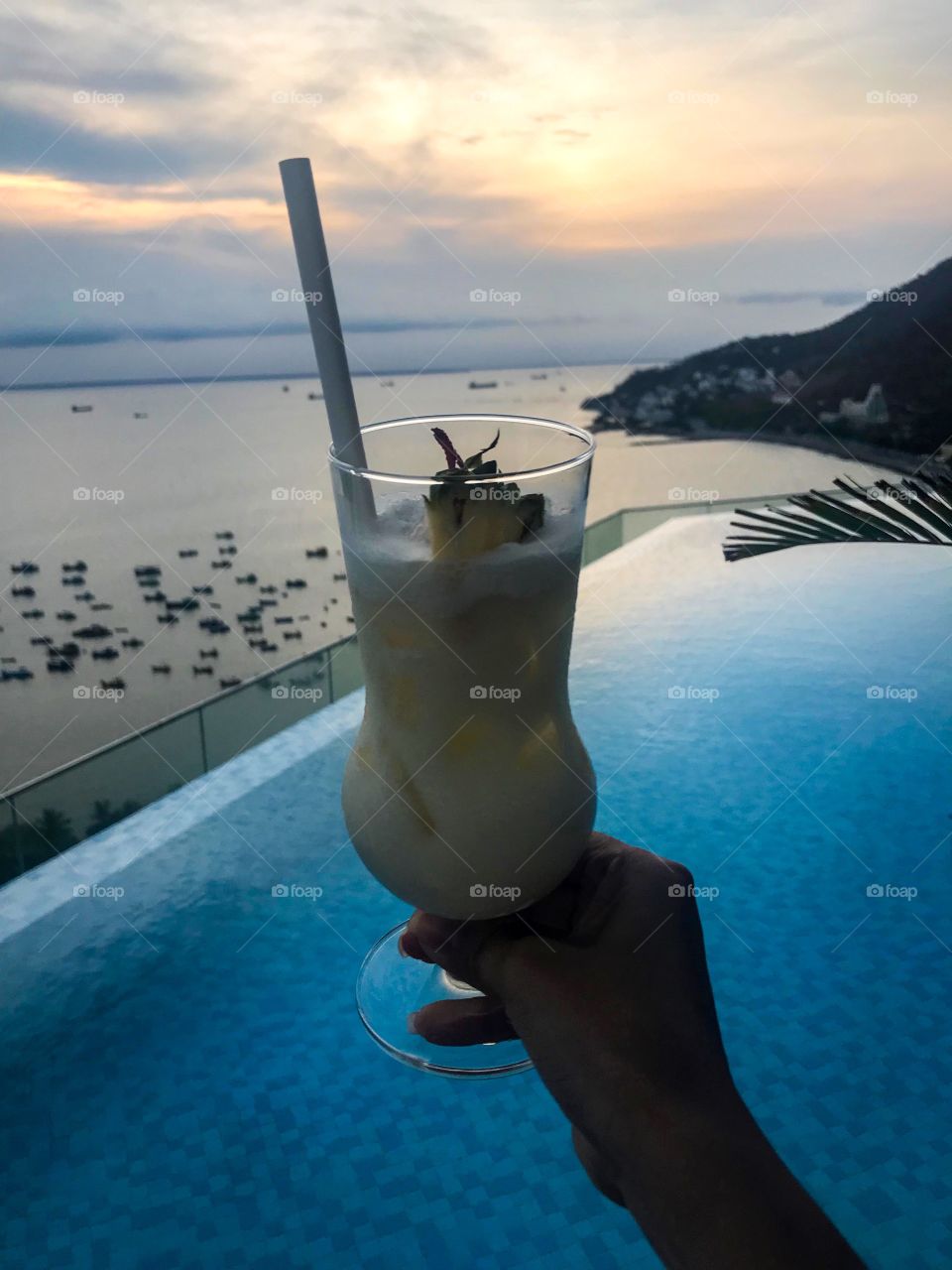 Enjoy the sunset at the rooftop swimming pool , hand is holding a cocktail and enjoy the sea breeze