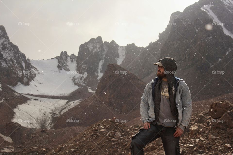 A man in a cap and a denim jacket stands on a glacier in the mountains