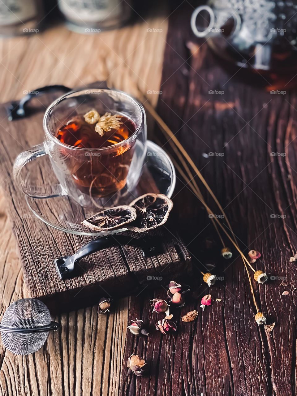 A cup of hot flower tea on a wooden board and some scattered dried flower beside it