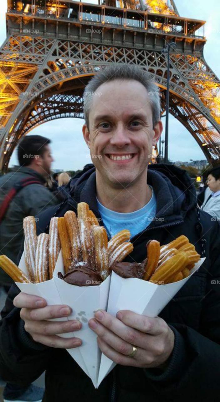 man with tasty churros and chocolate at
Eiffle tower, at dusk illuminated,   Paris,  France, eu, Europe

A churro is a fried-dough pastry—predominantly choux—based snack. Churros are popular in Spain, Portugal, France, the Philippines, Ibero-America and the Southwestern United States. In Spain, churros can either be thin (and sometimes knotted) or long and thick. They are normally eaten for breakfast dipped in champurrado, hot chocolate, dulce de leche or café con leche