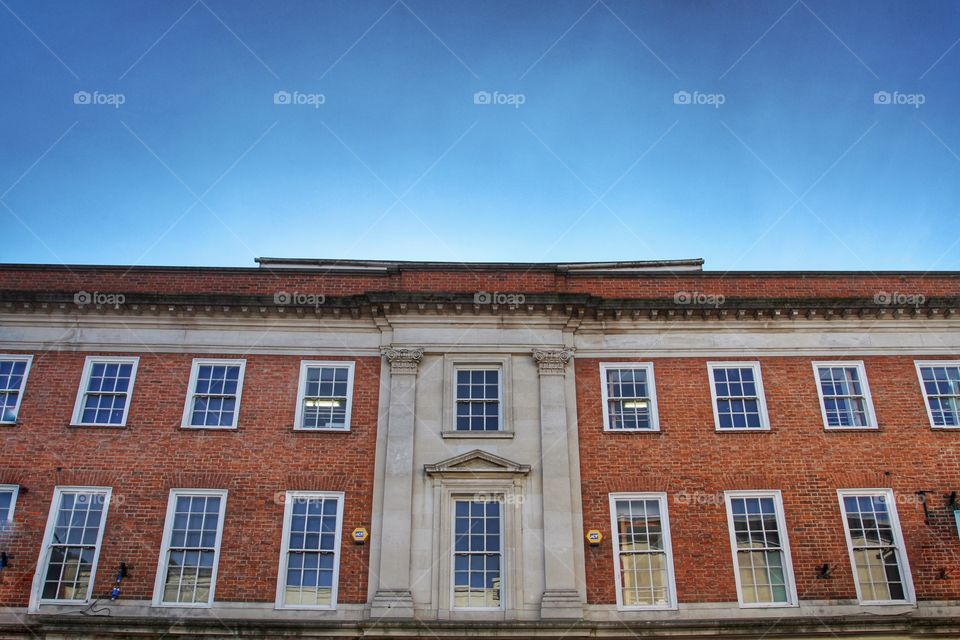 The facade of a grand brick building with uniform Windows and red brick.