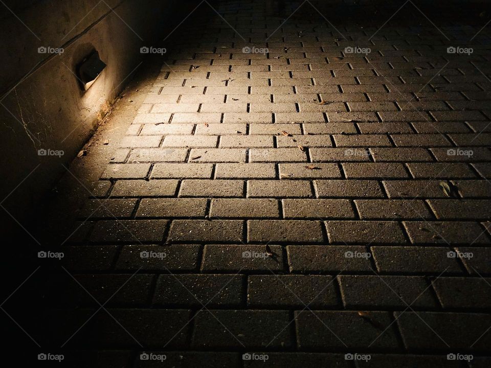 Rectangular paving stones in the light of the walkway, fade away into the dark night