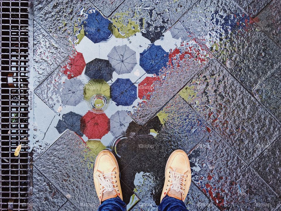 Reflection of colorful umbrellas in a rain puddle formation 