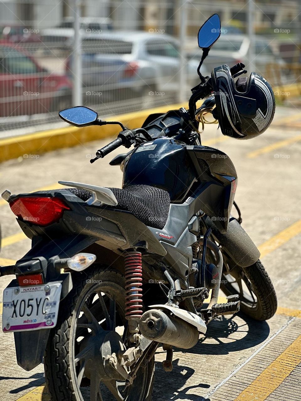 Black motorcycle parked in a parking lot with a helmet hanging on it, in a sunny day.