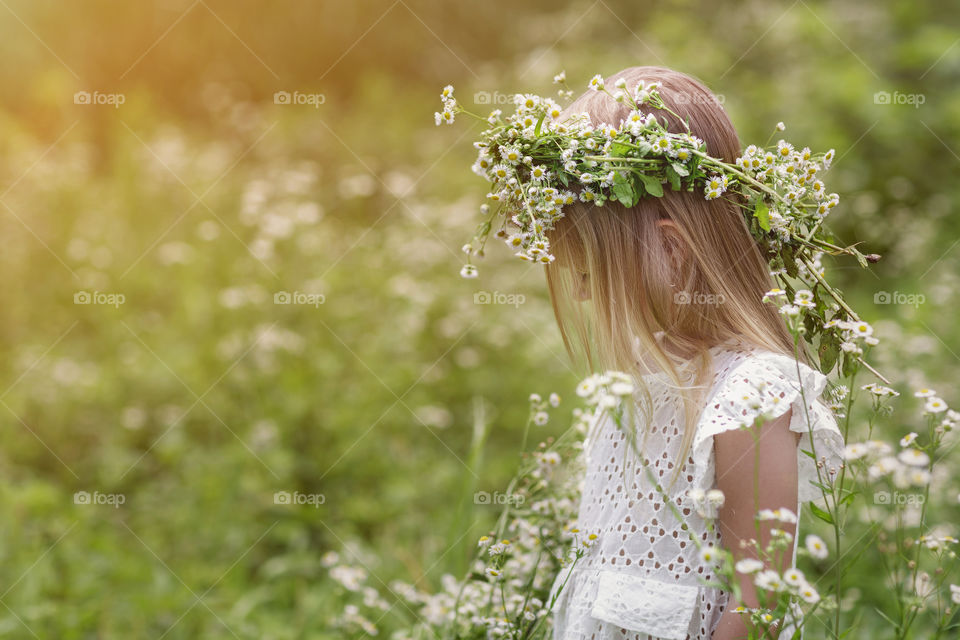 Kid in white dress stands on chamomile meadow 
