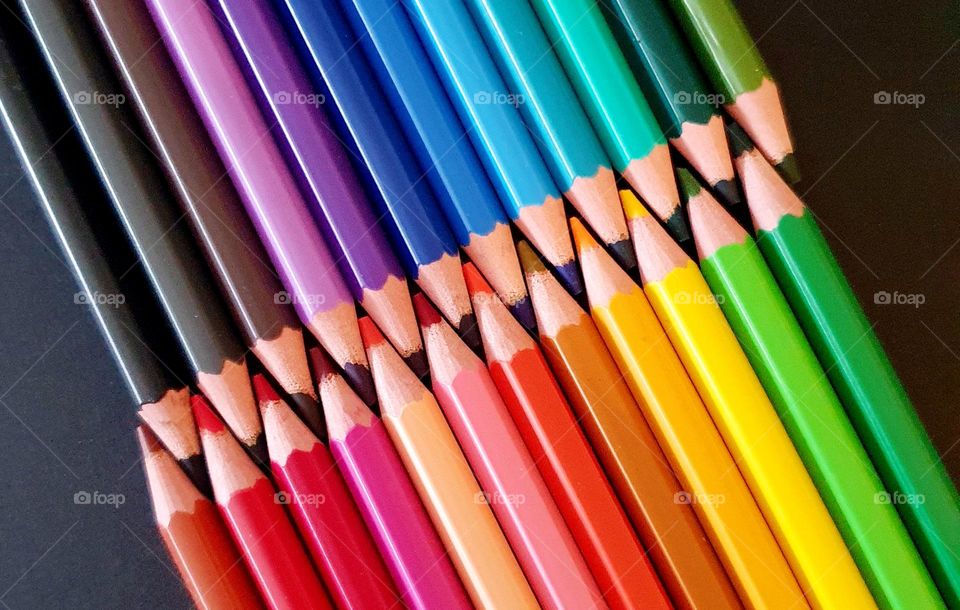 Colourful flatlay composition made of colour pencils placed on black paper showing two rows of pencil leads interlocked