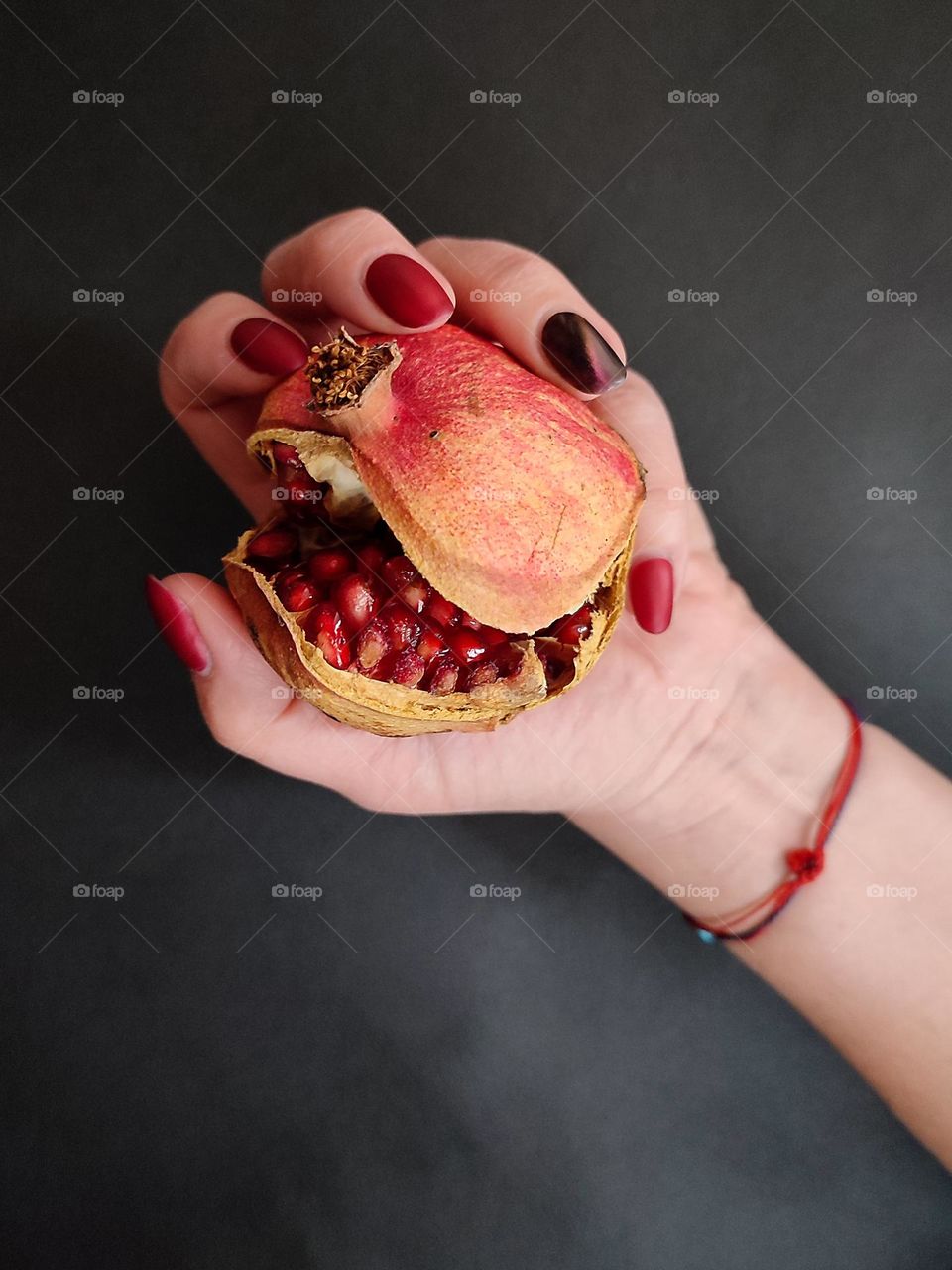 Beautiful female hand with nice art manicure holding a ripe pomegranate