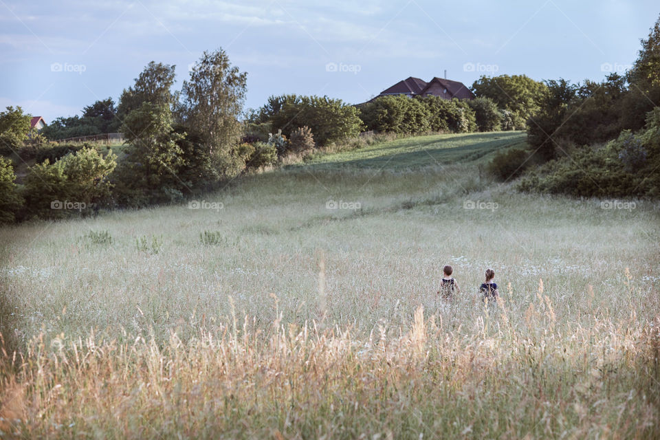 Little happy kids playing in a tall grass in the countryside. Candid people, real moments, authentic situations