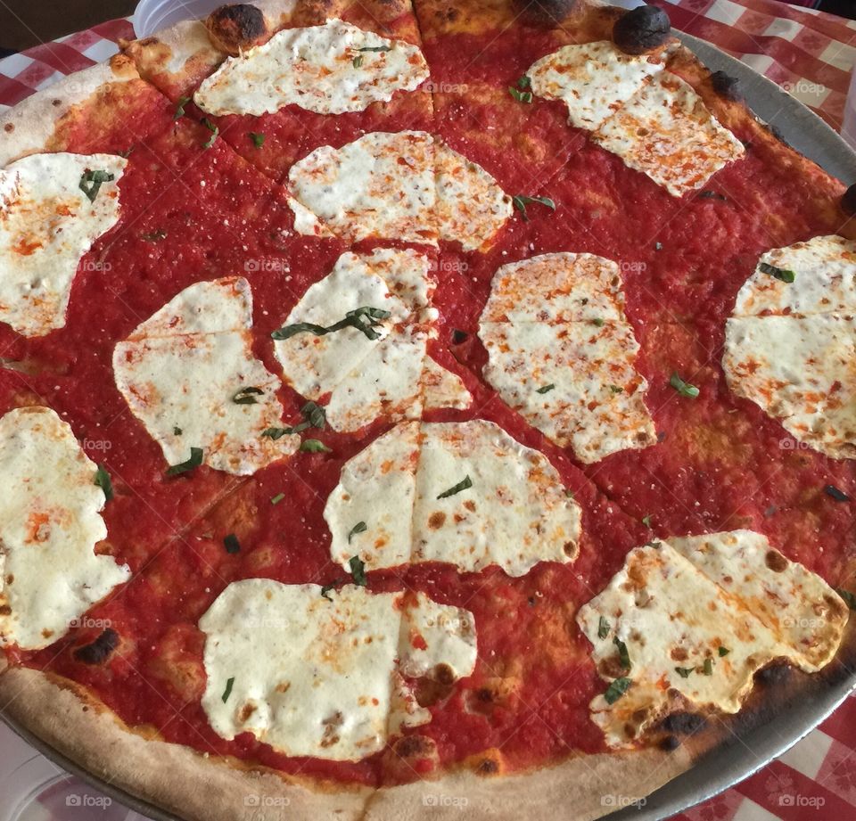 Hand tossed margherita pizza on red checkered tablecloth. 