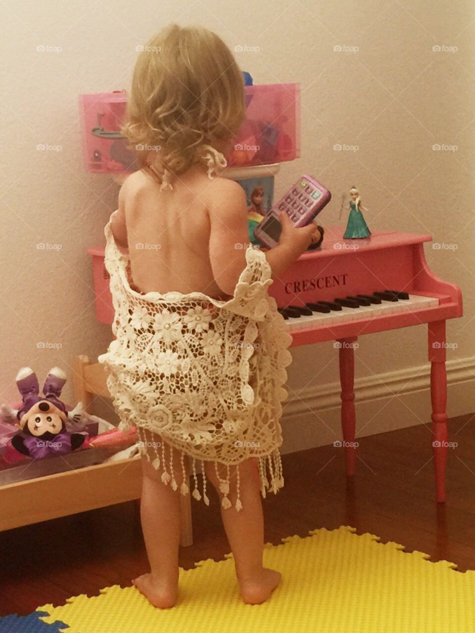 Toddler girl playing dress up in front of toy pink piano