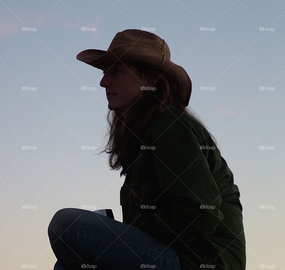 cowgirl chilling at dusk. sitting on a rock at dusk, chilling and thinking
