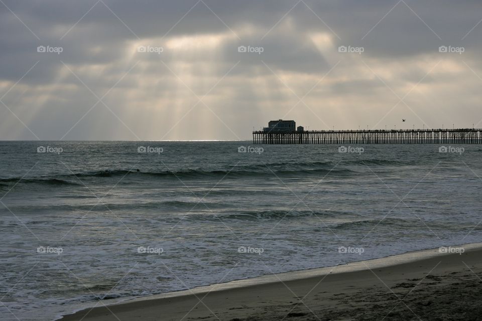 Standing on the beach looking out to the pier as the sun comes through the clouds