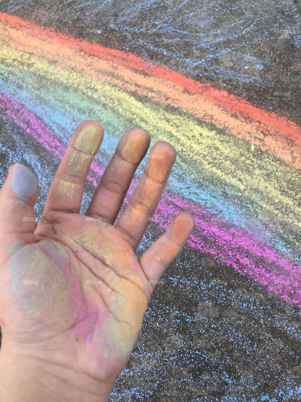 Hand with rainbow chalk, rainbow in background drawn with chalk