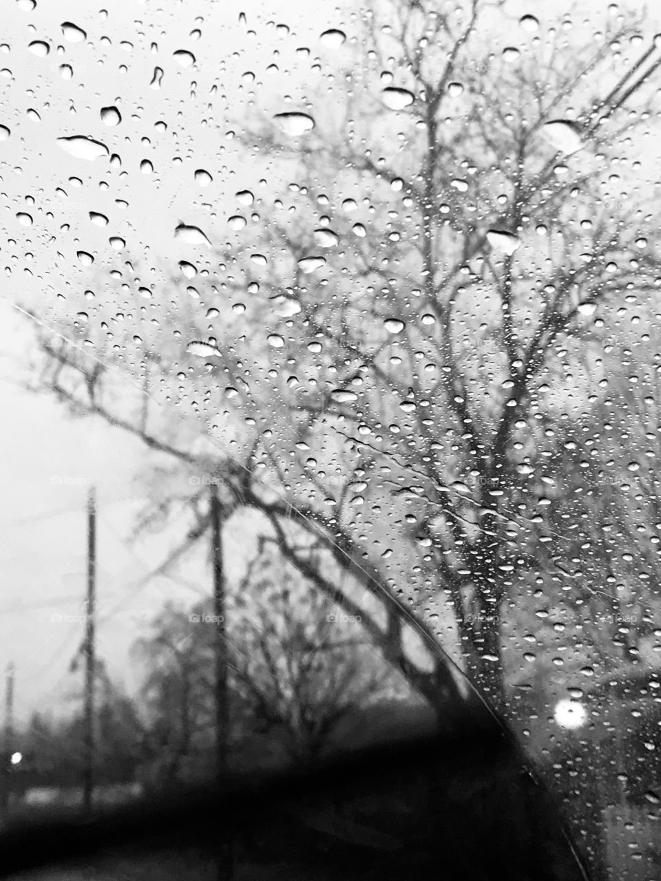 Black and white photo of Looking out side the car window at the rain drops pouring down from the cloudy gray sky, USA, America