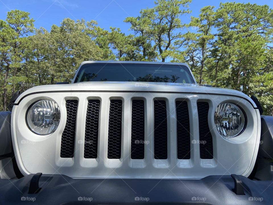 A view of the grille of my 2018 Jeep Wrangler Sport with trees and blue sky as a backdrop. Shot at Cattus Island Park in Toms River, NJ. 