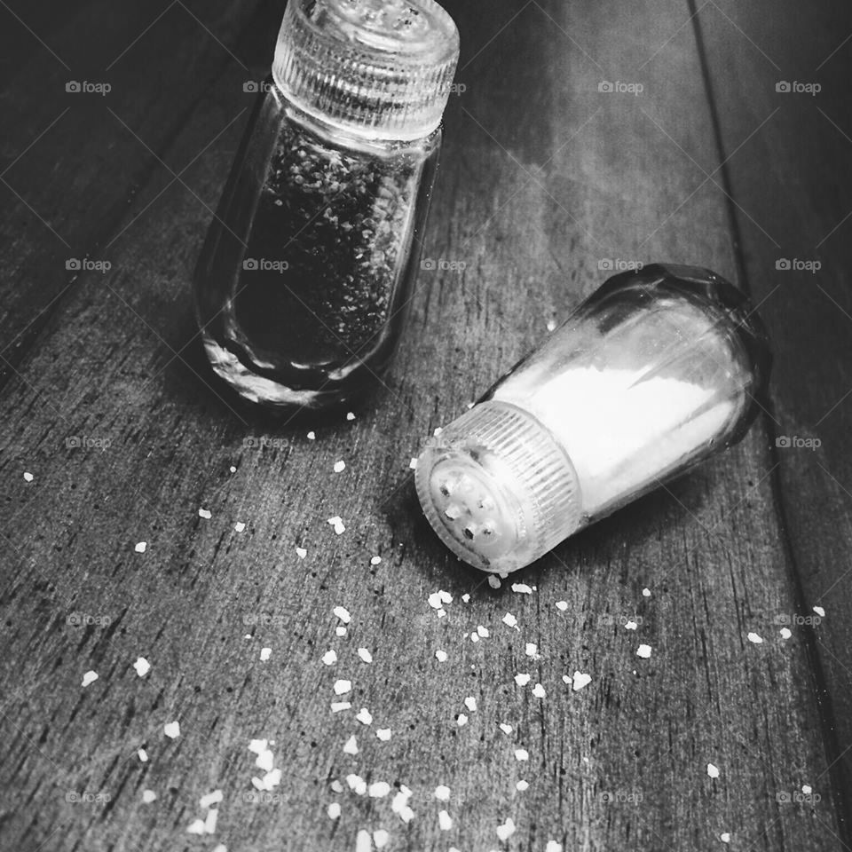 A pepper shaker next to a spilt salt shaker on barnwood.