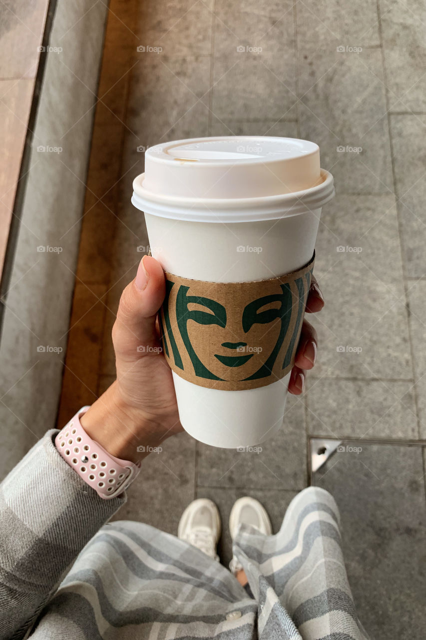 Trendy woman holding cup of coffee from Starbucks 