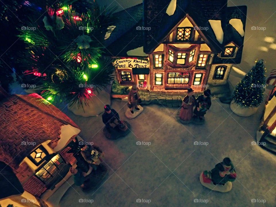 A Christmas village display with vintage shops, Christmas trees and lights and active people. 