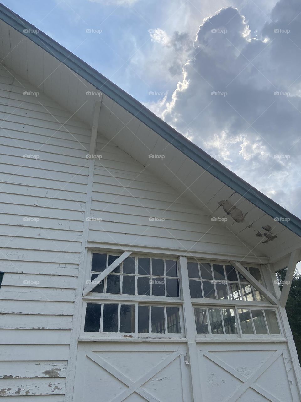 An angular view of a horse barn against the backdrop of a blue cloud-filled sky. This is part of a group of historic farm buildings at Thompson Park in Lincroft, NJ. At one time, Thoroughbred horses were bred and trained here.