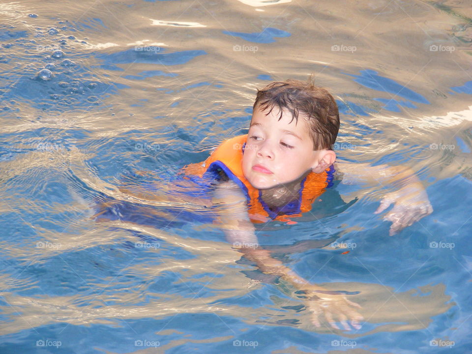 This boy is wearing a life vest and swimming in a pool.