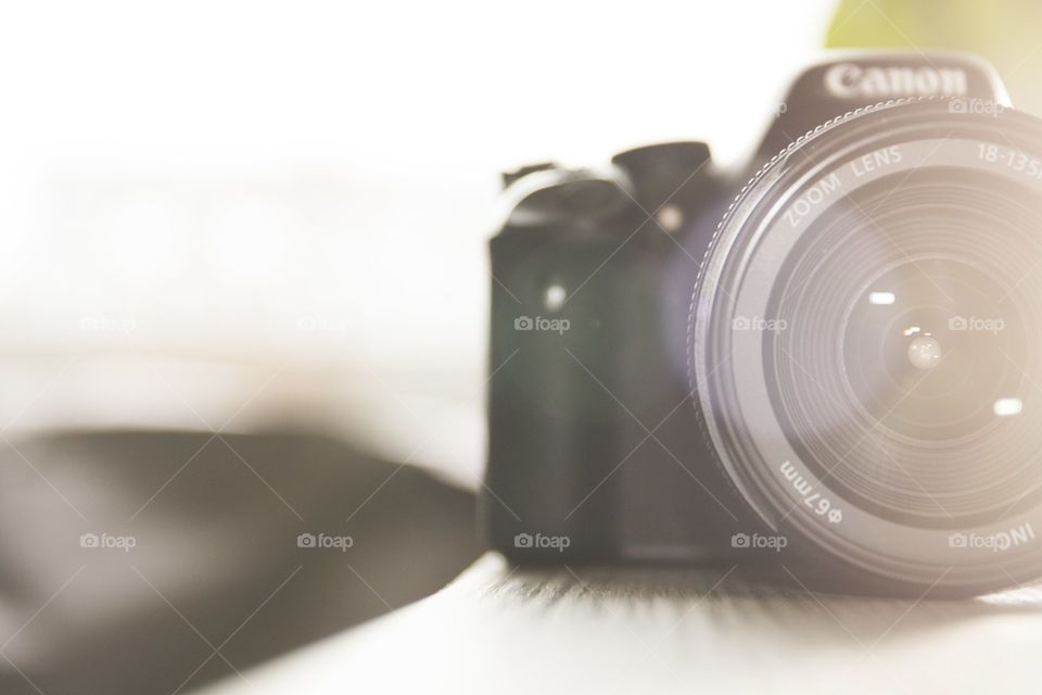 A portrait of a photo camera straight into its circular lens with some nice back lighting on a wooden table.